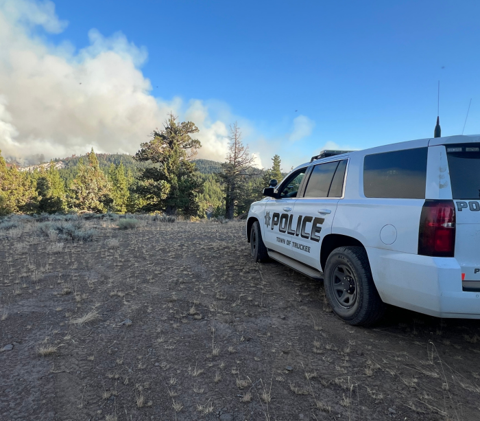 Police Car parked with a bloom of smoke from a fire in the distance over mountains. 
