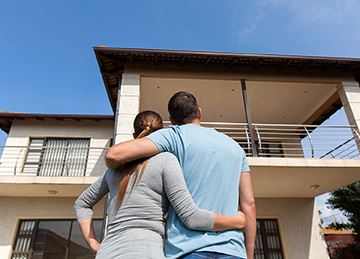 A couple faces toward an apartment building with their arms around each other
