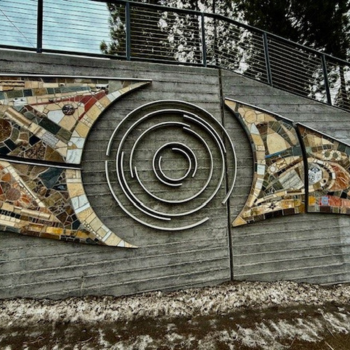 Close up photo of the PATH sculpture- an abstract shaped sculpture on a wall up a hill by a road.  