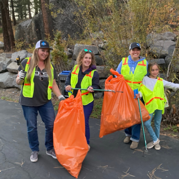 three adults and one child in yellow vests with orange trash bags and cleanup pinchers, smiling. 