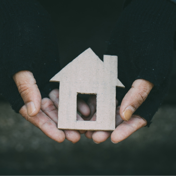 a person's hands in fingerless gloves holding a cut out house in cardboard. 