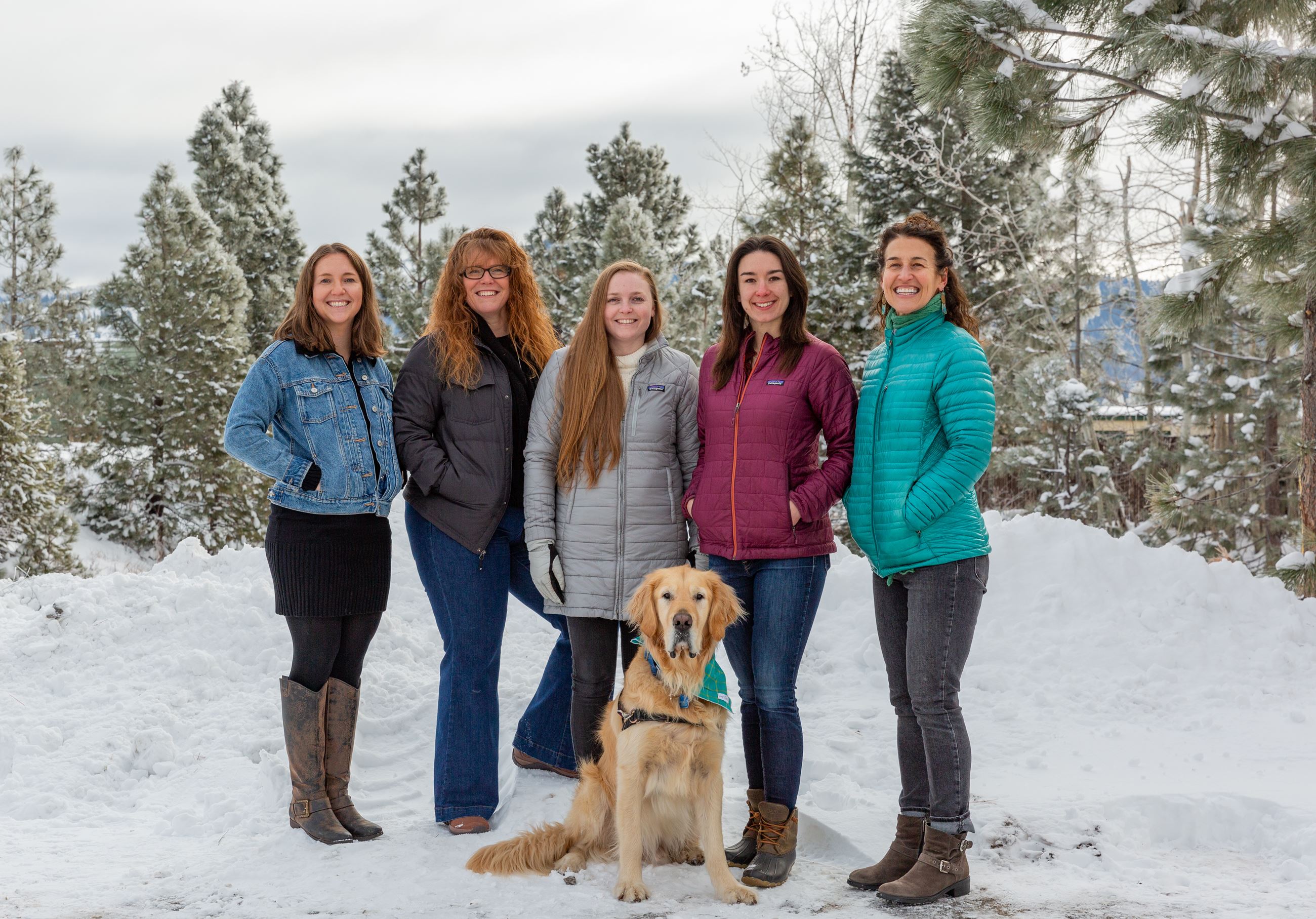 Five female staff members standing in the snow with a dog in the middle. 