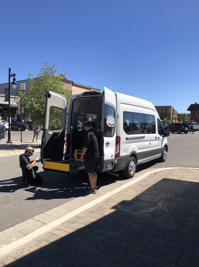 Two people at the back of a shuttle van pulling out the wheelchair ramp. 