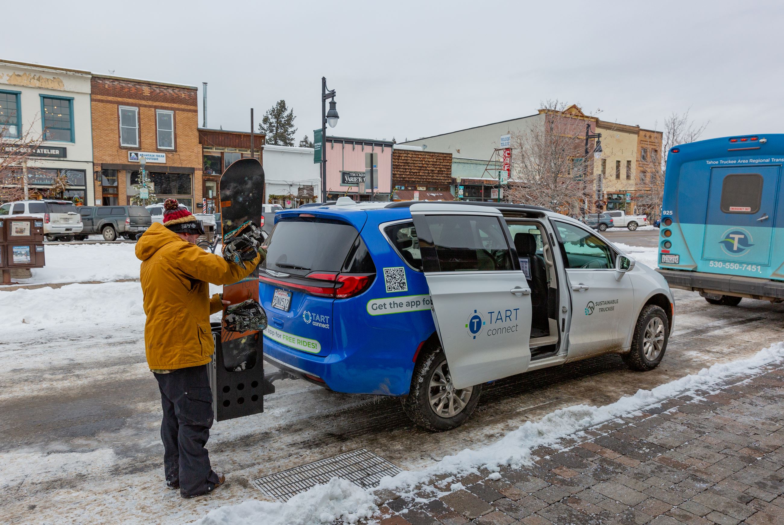 Person removing their snowboard from the ski rack at the back of van. 