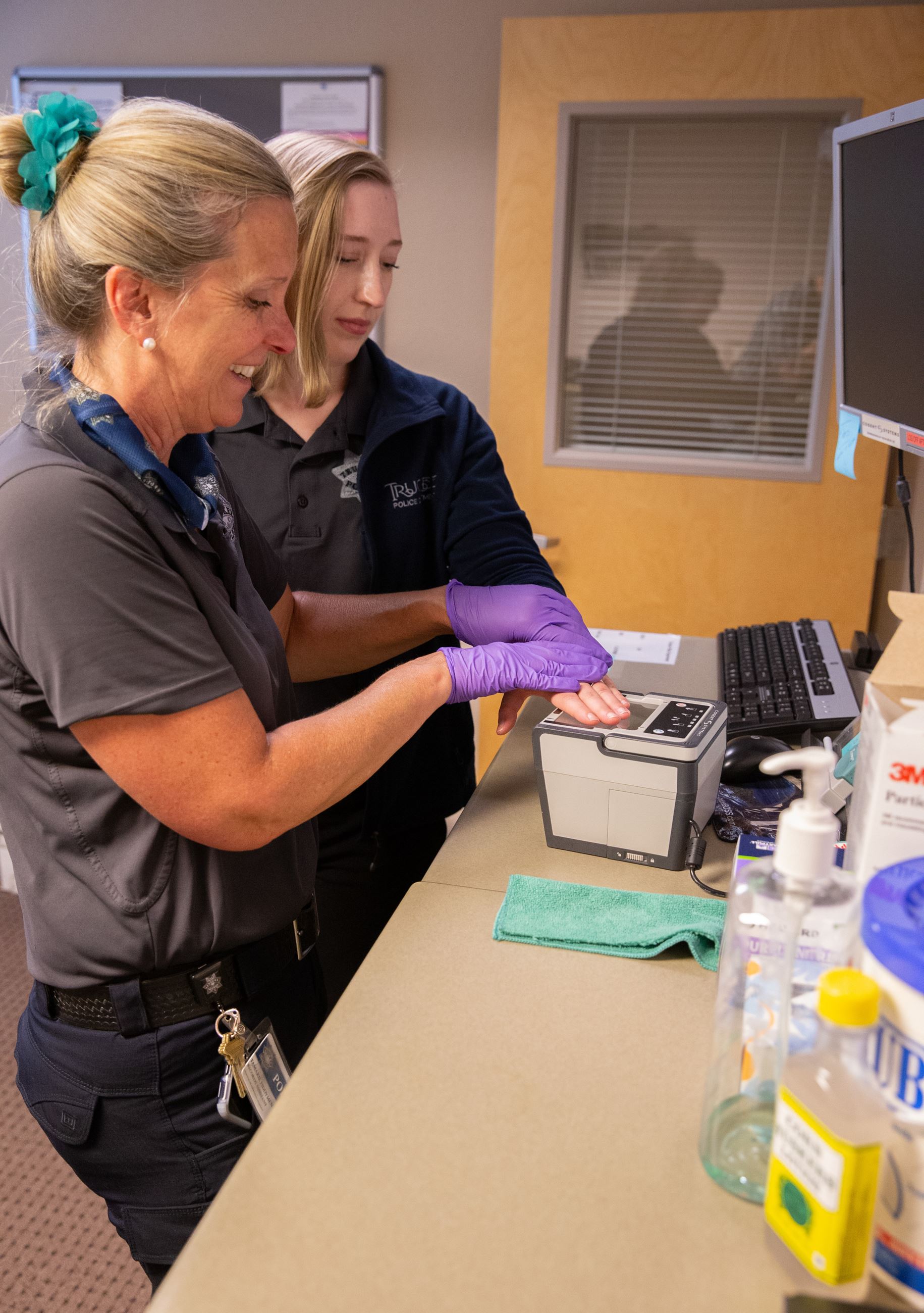 Two women in an office. One is scanning the others fingerprints. 