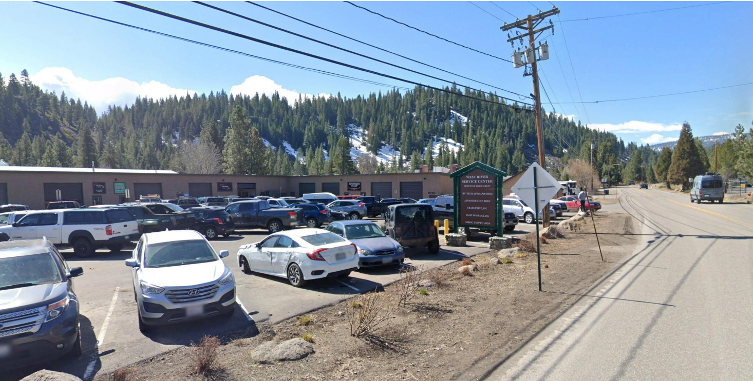 Photo of West River St parking lot full of cars with multiple businesses from street vie. 